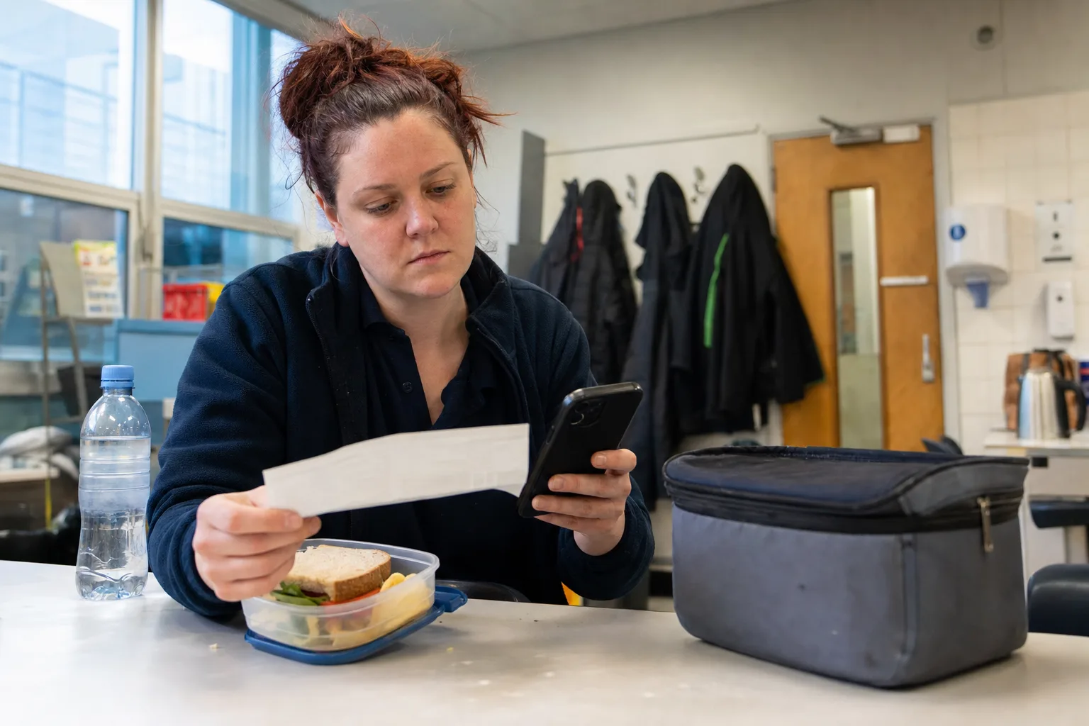 A supermarket worker checking a payslip and phone calculator during her break