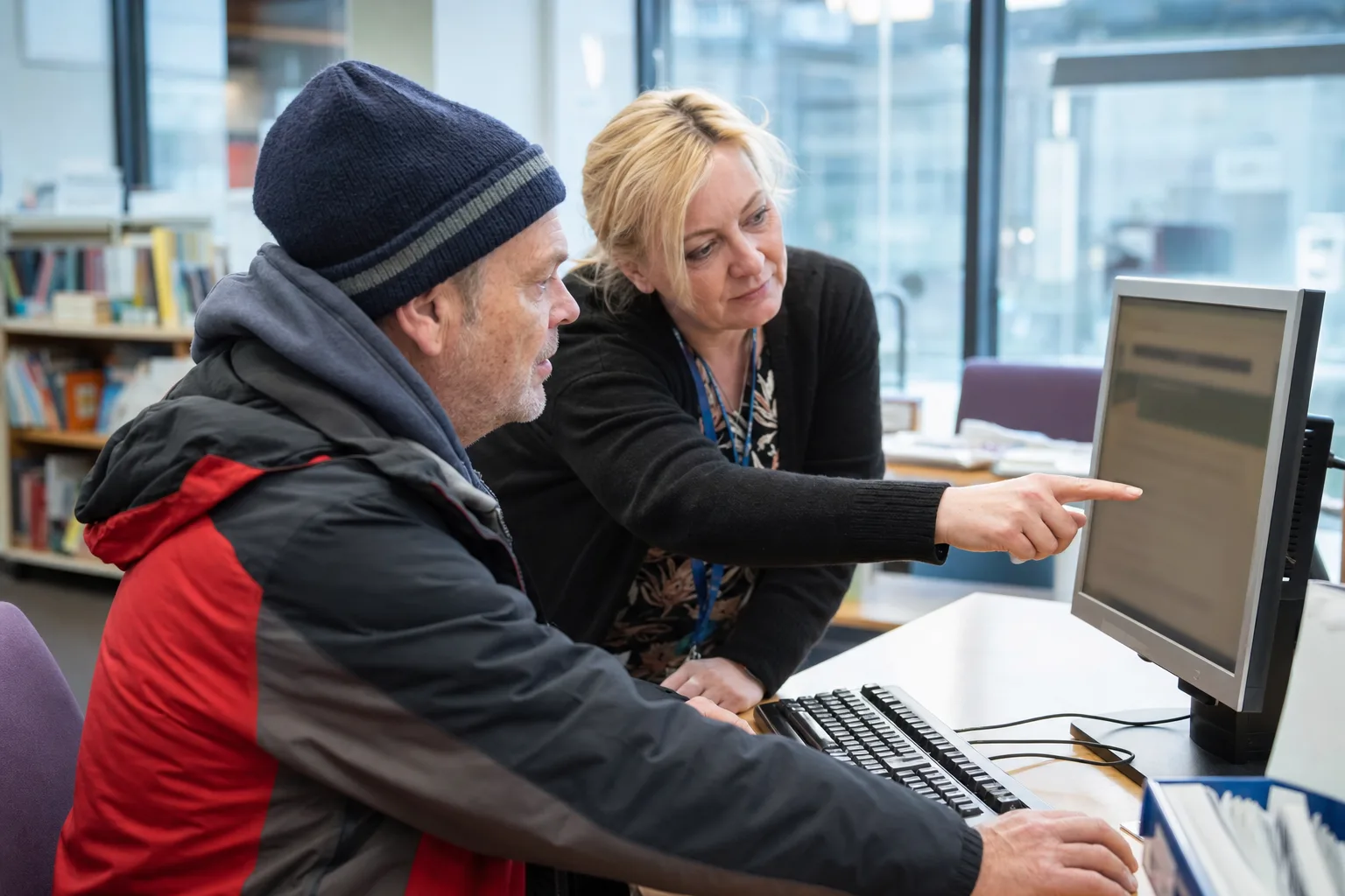 A community adviser helping a resident complete an online application at a public computer
